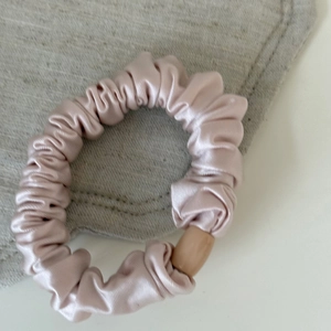 Detail view of pink satin scrunchie with soft pleats and decorative wooden buckle fastener