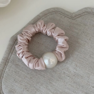 Detail shot of a soft champagne pink satin scrunchie with elegant large white pearl