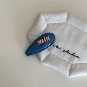 Detail shot of a blue teardrop hair clip with a red and white 3D min letter ornament