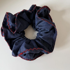 Détail d'un chouchou en denim bleu avec surpiqûres décoratives rouges sur les bords