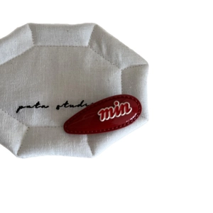 Elegant red teardrop hair clip with white lettering on a textured white display pad