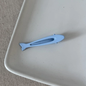 Dettaglio della clip per capelli a forma di pesce azzurro con texture opaca su vassoio