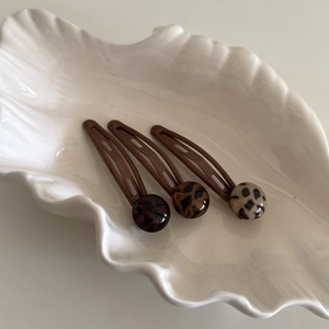 Three-piece leopard print BB hair clips in chocolate, caramel, and cream tones on a white shell plate