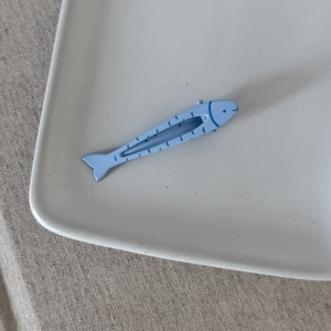Dettaglio di un fermaglio per capelli a forma di pesce blu su un vassoio di ceramica