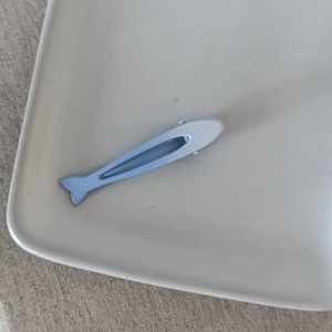 Dettaglio della molletta per capelli a forma di pesce azzurro su piatto di ceramica bianca