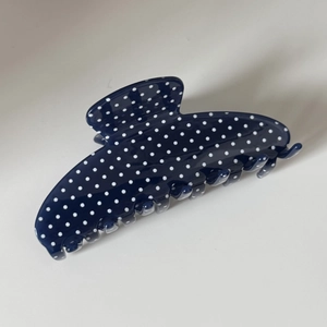 Close-up of navy blue hair claw clip with white polka dots and glossy finish texture