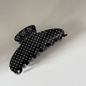 Close-up of a large black acetate hair claw clip with white polka dots and metal hinge