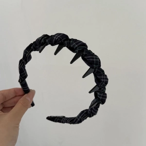 Detail of navy plaid headband with black punk spikes shown on a minimalist background