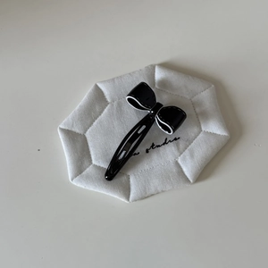 Barrette à cheveux élégante en acétate noir avec bordure blanche sur fond minimaliste blanc