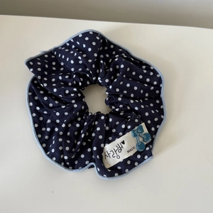 Close-up of navy blue polka dot fabric scrunchie with cherry charm and Korean label