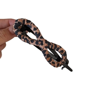 Vintage leopard print hair clip with bow shape held by hand over a white background