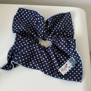Detail of navy blue polka dot scrunchie with light blue cherry charm and woven label