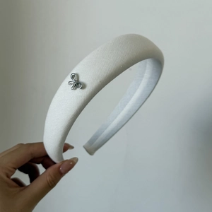 Detail of white padded headband featuring a delicate silver metal bow accessory