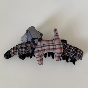 Close-up of fabric hair claw clip featuring a plaid plush dog toy with red and blue pattern