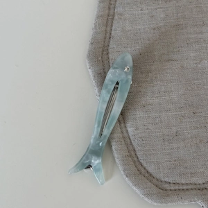 Detail of fish-shaped acetate hair clip with marble texture and rhinestone eye accent