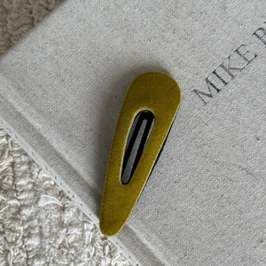 Detailed close-up of mustard yellow flocked triangular snap hair clip on a book
