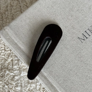 Close-up of a matte dark brown teardrop snap hair clip on a textured fabric book surface