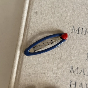 Detail of navy blue oval hair clip with red heart on textured book background