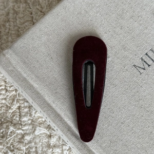 Close-up of a burgundy velvet snap clip with a teardrop shape on a minimalist box
