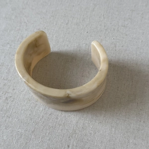 Close-up of wide ivory marble resin cuff bangle with smooth rounded edges on grey fabric