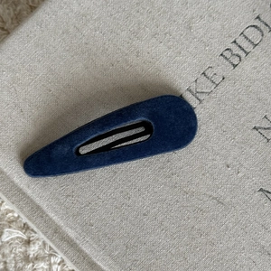 Detail view of navy blue velvet-flocked drop hair clip on neutral textured background