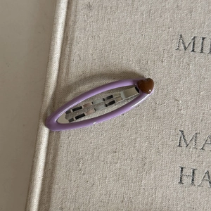 Close-up of a purple oval metal hair clip with a small brown heart on a beige background