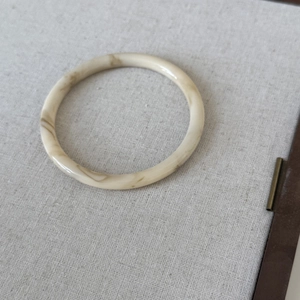 Detail view of a beige resin bangle with brown marble texture on a textured fabric