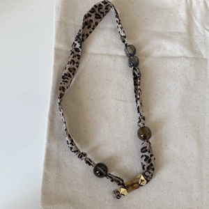 Detail of leopard print silk scarf necklace featuring dark marble beads and gold rivets