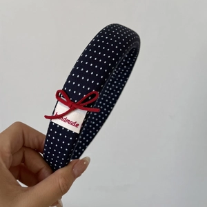 Détail d'un serre-tête bleu marine à pois avec un nœud rouge fait main et étiquette