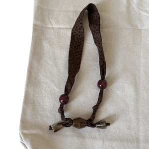Brown leopard print silk scarf necklace with vintage beads on a beige fabric background