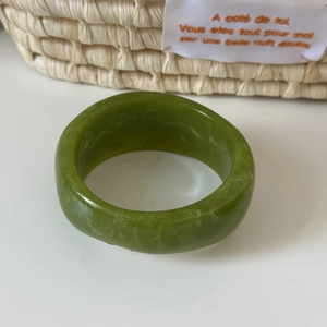 Close-up of green acrylic resin bangle with white marbled texture on white surface