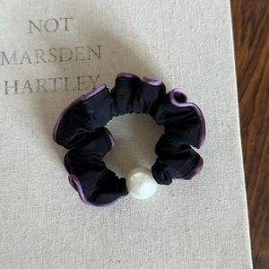 Detailed close-up of a black ruffled scrunchie with purple edges and a large faux pearl