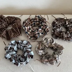 Close-up of five plaid bow scrunchies in brown and grey tones on beige fabric