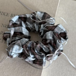 Detail view of coffee plaid scrunchie with grey satin bows on a beige book background