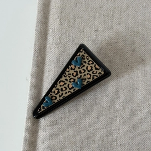 Detail of leopard print triangle hair clip with 3D blue heart accents on canvas