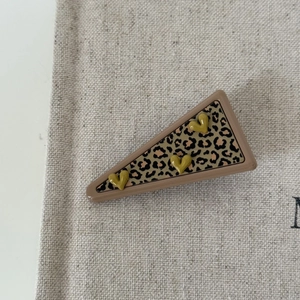 Detail of a triangle hair clip with leopard print and 3D yellow hearts on beige canvas