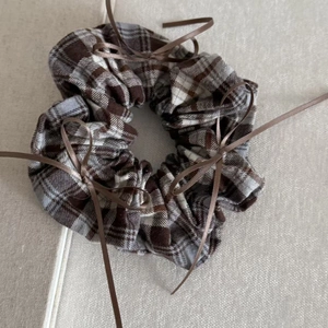 Macro detail of brown plaid scrunchie with long satin ribbons on linen background