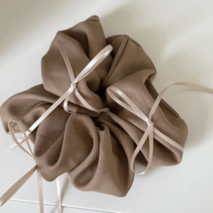 Detail of coffee brown scrunchie with satin bows and twill fabric texture on white surface
