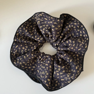 Deep purple scrunchie with gold leopard pattern and black stitched edges in flat lay view