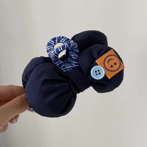 Détail de la pince à cheveux en tissu bleu foncé avec étiquette smiley et bouton déco