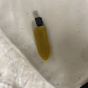 Détail d'une pince à cheveux en velours jaune moutarde sur un plateau en céramique