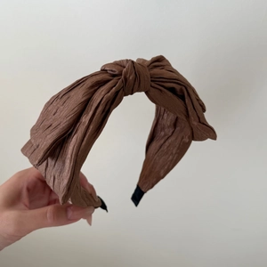 Close-up of brown pleated bow headband showing fine fabric texture and knotted style
