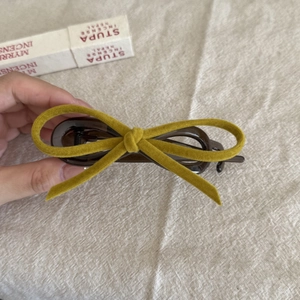 Detail view of mustard yellow velvet bow hair clip with dark brown acrylic base