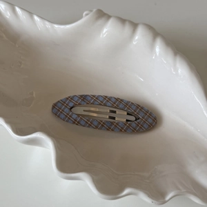 Barrette à cheveux ovale en tissu à carreaux bleu et marron sur une assiette en coquille