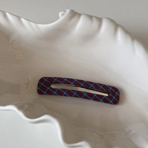 Gros plan d'une pince à cheveux rectangulaire à carreaux rouges et bleus sur plat