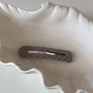 Détail d'une pince à cheveux BB à carreaux bleu et marron sur une assiette en coquille
