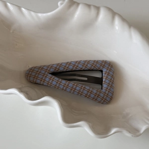 Détail d'une pince à cheveux vintage à carreaux bleu et marron sur un plateau coquille