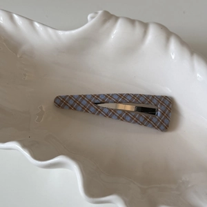 Détail d'une barrette vintage à carreaux bleus et marrons sur un plateau en céramique