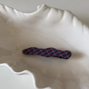 Détail d'une pince à cheveux à carreaux rouge et bleu sur un plateau en céramique