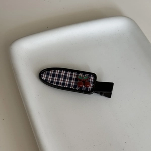 Detail of red cherry plaid hair clip on white tray featuring matte black duckbill base
